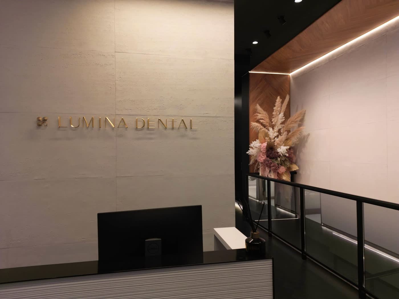 Lumina Dental's reception in Ultimo — travertine wall with brass lettering and dried florals